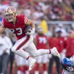 San Francisco 49ers running back Christian McCaffery (left) scored a 4-yard touchdown in the second quarter against the New York Giants on Thursday night at Levi's Stadium, tying him with 49ers legend Jerry Rice for most touchdowns scored in consecutive games (12), a record Rice had held alone since the 1987 season. With a touchdown next week against Arizona, of course, McCaffery could own the record alone. (Photo courtesy of YARDBARKER.COM)