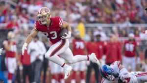 San Francisco 49ers running back Christian McCaffery (left) scored a 4-yard touchdown in the second quarter against the New York Giants on Thursday night at Levi's Stadium, tying him with 49ers legend Jerry Rice for most touchdowns scored in consecutive games (12), a record Rice had held alone since the 1987 season. With a touchdown next week against Arizona, of course, McCaffery could own the record alone. (Photo courtesy of YARDBARKER.COM)