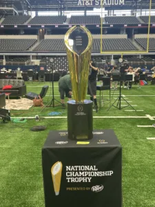 The College Football Playoff National Championship Trophy (above), sitting at A&T Stadium during the Big 12 Media Days in July. The first CFP rankings were released Tuesday night, and Ohio State is number one; defending champion Georgia, number one in the other polls, is number two. (Photo by CLAYTON FLETCHER)