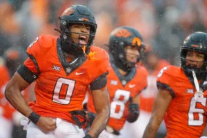 Oklahoma State running back Ollie Gordon (0) helps get his teammates pumped up after making a big play. Gordon leads the nation in rushing yards, is among the leaders in most rushing categories, and he and the Cowboys (9-3) will face the Texas Longhorns (11-1) on Saturday at 11 a.m. on ABC in the Big 12 Conference Championship Game at AT&T Stadium. (Photo courtesy of THE OKLAHOMAN)