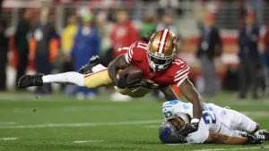 San Francisco receiver Brandon Aiyuk (left) makes a catch off a ball that bounced off the helmet of Detroit Lions defensive back Kindle Vildor, a 51-yard gain that sparked the 49ers' 17-point comeback. San Francisco will be the NFC's representative in Super Bowl LVIII on Feb. 11, against Kansas City. (Photo courtesy of FOX NEWS)