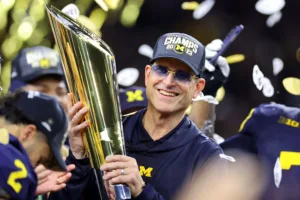 Michigan coach Jim Harbaugh hoists the College Football Playoff national title trophy after beating Washington on Jan. 8. (Photo courtesy of NYPOST.COM)
