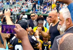 Dwayne "The Rock" Johnson talks to a youth football team just before kickoff of Saturday's Birmingham-Arlington UFL opener in Arlington. Johnson, a partner in the ownership of the new spring league, welcomed fans to Choctaw Stadium for the first UFL game. The 10-game season continues on Sunday. (Photo by JENNA LUCAS - THEFOOTBALLBEAT.COM)